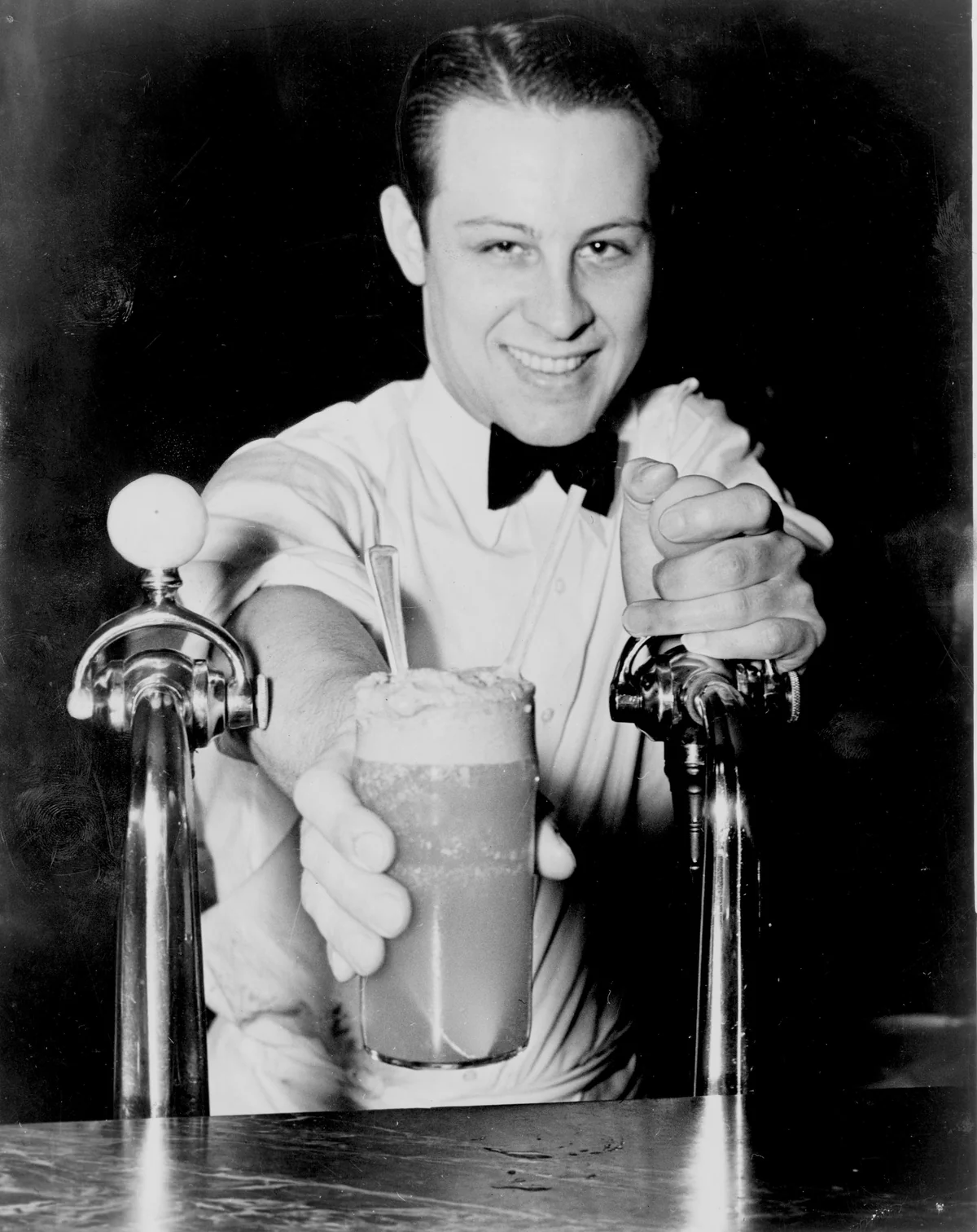 Soda jerk passing ice cream soda between fountains, 1936